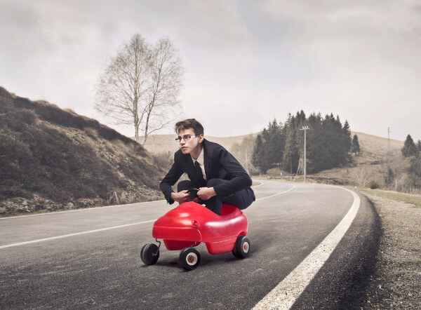 Hypnotised man imaginging he is hunched into a toy childs racing car on an empty road