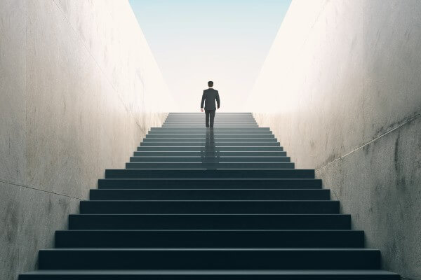 Metaphorical image of a hypnotherapy client walking up a long staircase towards a bright light, which represents their goal success.