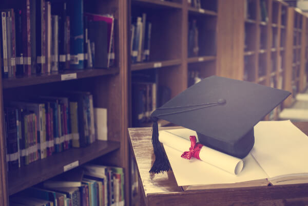 Hypnotherapy certificate on a pile of books next to a mortarboard hat in a library.