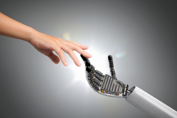 Human hand reaching out and finding a robot hand reaching back.